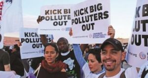 Multiple people at a rally holding signs that read Kick Big Polluters Out