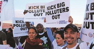 Multiple people at a rally holding signs that read Kick Big Polluters Out