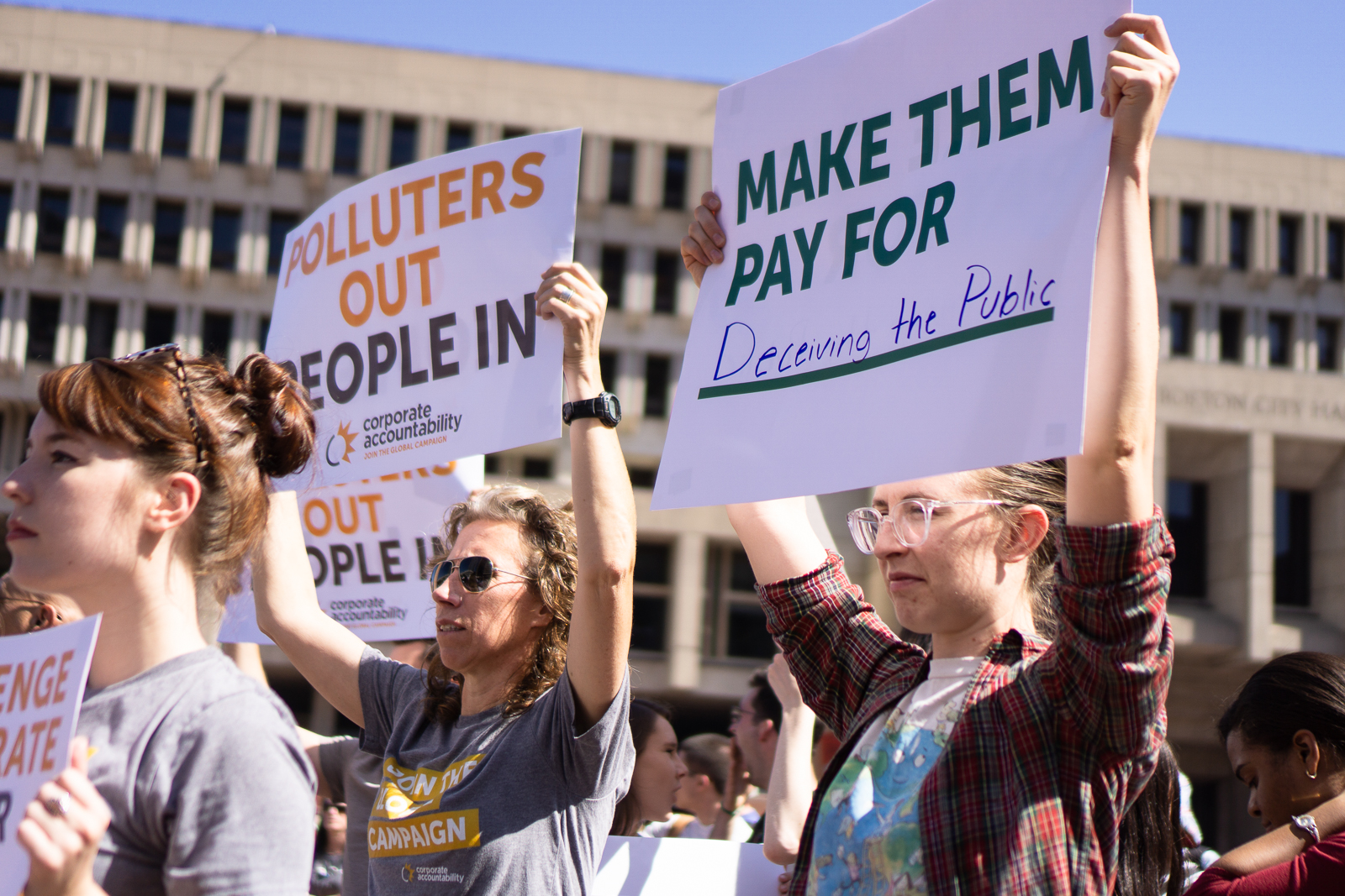 Two people at a climate protest holding signs: “Polluters Out, People In” and “Make them pay for deceiving the public.”