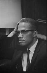 A black and white photo of Malcolm X resting his head against his hand.