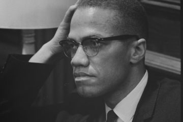 A black and white photo of Malcolm X resting his head against his hand.