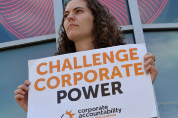 Corporate Accountability organizer holds sign that reads "Challenge Corporate Power